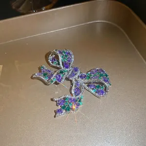 Sparkling zircon bow brooch with purple and green stones on a gold textured tray