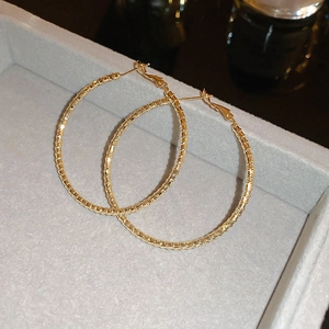 Macro view of gold-plated bamboo texture hoop earrings on a grey velvet tray