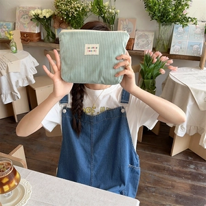 Pale green corduroy makeup bag held by a model in a cozy cafe setting with flowers