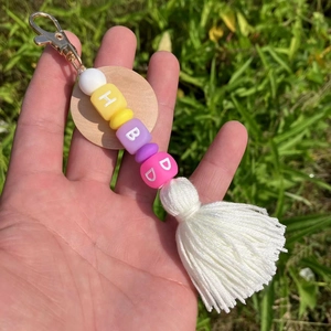 Détail d'un porte-clés fait main avec perles de lettres, pompon blanc et disque en bois