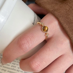 Close-up of gold plated tiger eye ring with star accents held by a hand near coffee
