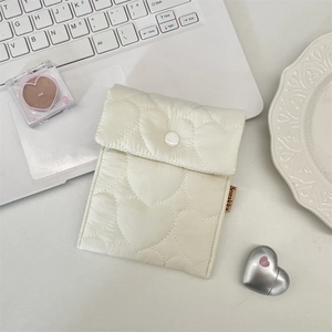 Close-up of cream quilted heart pattern pouch with button closure on a laptop