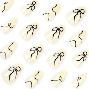 Artistic short almond press-on nails with black bow patterns and minimalist stripes
