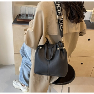 Detail of black pebbled leather bucket bag with patterned wide fabric strap on a model