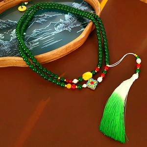 Détail d'un long collier de perles vert foncé avec pampilles et charme floral