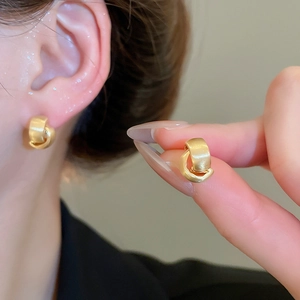 Detail showing brushed gold C-shape stud earrings worn on ear and held by fingers
