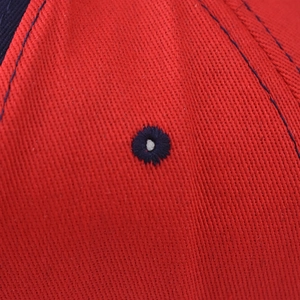 Détail macro de l'œillet brodé respirant sur la casquette de baseball en coton sergé rouge