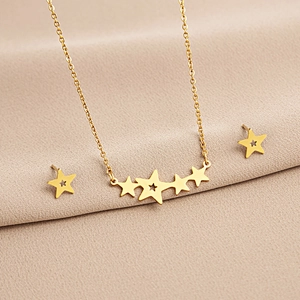 Detail shot of a gold star necklace and earrings set on a soft beige fabric background