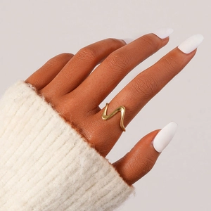 Anello dorato minimalista con linee ondulate indossato con un maglione beige