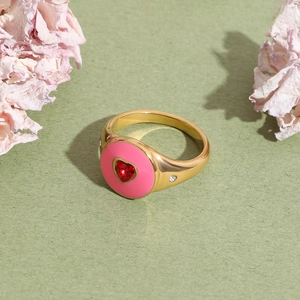 Close-up of golden 18K stainless steel ring with pink enamel and red heart-shaped gemstone
