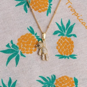 Collier avec pendentif ourson doré et zircons brillants sur fond de tissu tropical