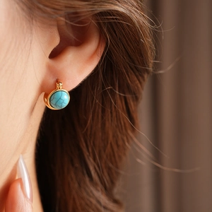 Détail d'une boucle d'oreille vintage en or avec résine verte portée par un mannequin