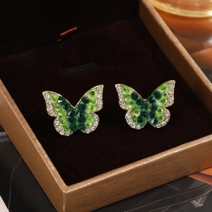 Close-up of golden butterfly earrings with green crystals and sparkling white rhinestones