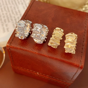 Macro shot of gold and silver irregular textured hoop earrings with a pleated metal surface