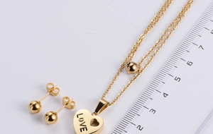 Macro view of gold titanium steel heart pendant with LOVE engraving and round bead earrings