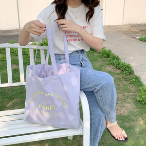 Outdoor lifestyle shot of a lavender canvas tote bag with yellow embroidery and Paris text