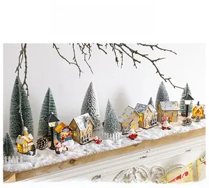 Detail of glowing wooden Christmas cottage set with snowy trees on a fireplace mantel