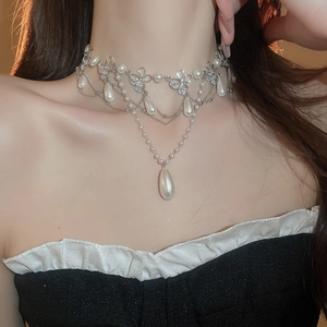 Close-up of multi-layer silver necklace with pearl bow and teardrop pendant