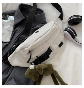 White canvas sling bag with black strap and olive green plush puppy keychain detail