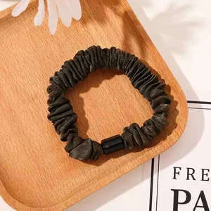 Detail of dark green satin scrunchie with a sleek black buckle on a wooden tray