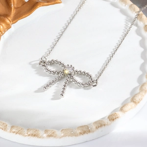 Close-up of silver bow pendant with central crystal on white ceramic plate