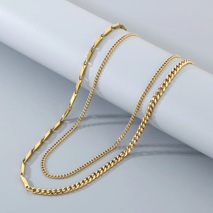 Detailed view of layered gold Cuban link necklaces on a white cylindrical display stand