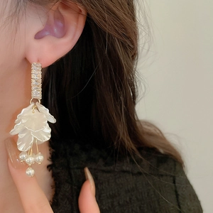 Detail of long drop earrings featuring white shell flower petals and pearl tassels on model