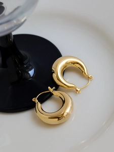 Macro shot of gold chunky hoop earrings with polished finish on a white ceramic tray