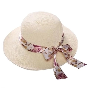Detail of cream straw sun hat featuring a purple floral ribbon bow on white background