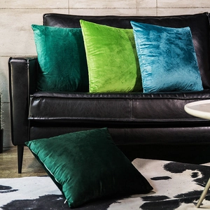 Detailed view of velvet cushion covers in green tones on leather sofa and cowhide rug