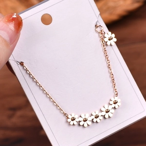 Detail of 18k gold daisy necklace with five small floral charms on a white display card