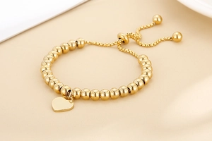 Detailed close-up of golden beaded bracelet featuring a heart pendant and adjustable slider