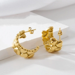 Detailed view of gold heart-shaped hoop earrings on a minimalist white stone pedestal