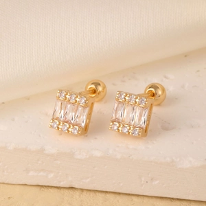 Macro shot of gold rectangle earrings with sparkling zircon stones on a white silk base