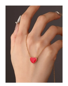 Close-up of a red heart pendant necklace on a delicate gold chain worn on the hand