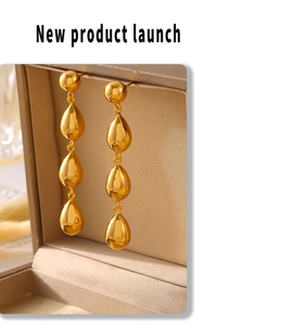 Close-up of golden geometric water drop tassel earrings on a beige velvet jewelry box
