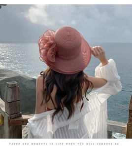 Pink organza sun hat with large floral detail shown against a scenic beach backdrop