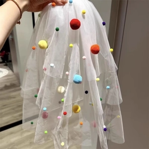 Detail of white tulle veil featuring colorful pom-pom decorations for party styling