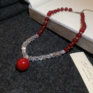 Detailed view of zircon pearl beaded necklace with red crystal pendant on tweed