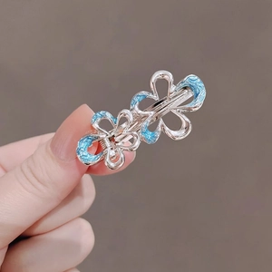 Silver flower hair clip with blue enamel detail held by fingers on grey background