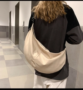 Rear view of a model wearing a beige nylon crescent bag in a tiled corridor setting
