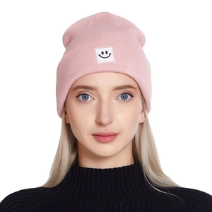 Pink knitted beanie hat for women featuring a minimalist smiley face patch and ribbed texture