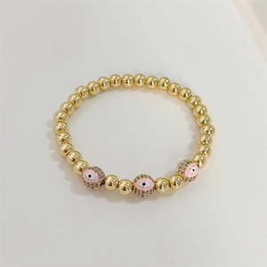 Macro view of gold beaded bracelet featuring three pink evil eye charms with micro-pave crystals
