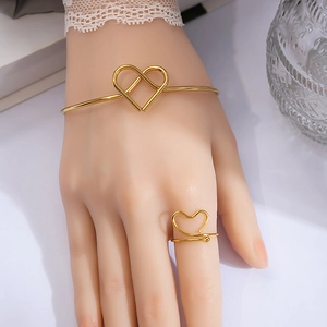 Detail of minimalist gold heart-shaped ring and open bangle set on a model's wrist