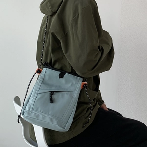 Detail of light blue messenger bag with rope strap and orange buckles on model