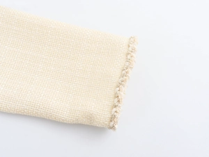 Dettaglio del tessuto in tweed crema con trama intrecciata e bordi sfilacciati