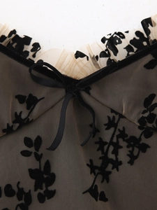 Détail du décolleté en mesh noir avec motifs floraux dévorés et petit nœud doux