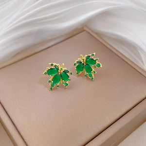 Macro view of golden maple leaf earrings featuring green gemstones on silk background