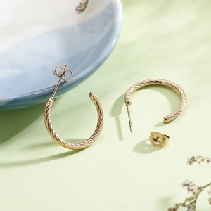 Detailed view of golden twisted hoop earrings with butterfly backs on a ceramic dish