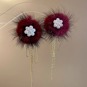 Macro shot of burgundy pompom earrings with pearl flower and golden chain tassels